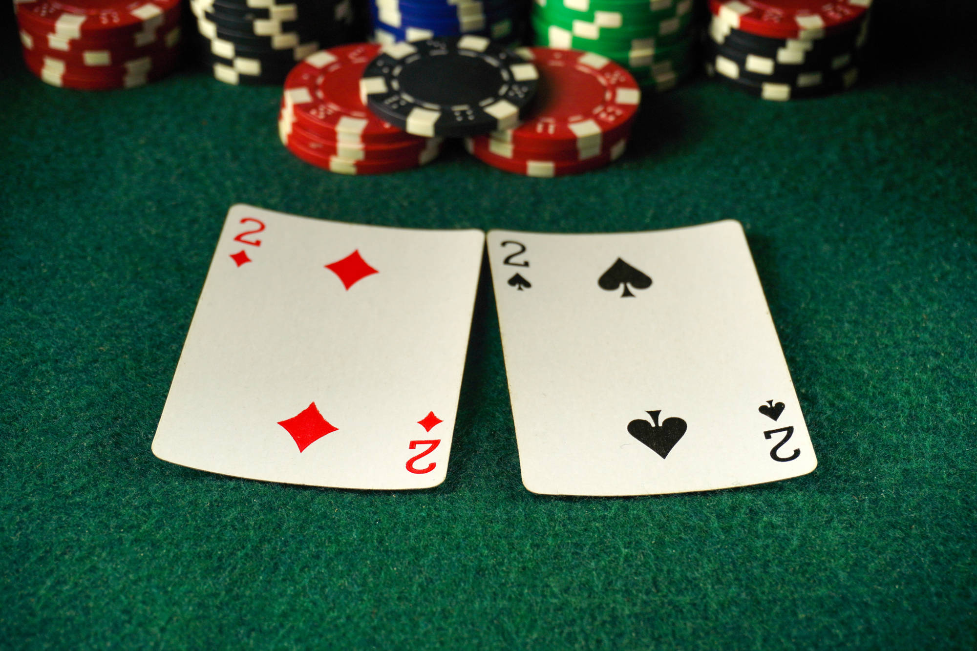 wo cards showing the 2 of diamonds and 2 of spades are placed on a green felt poker table.